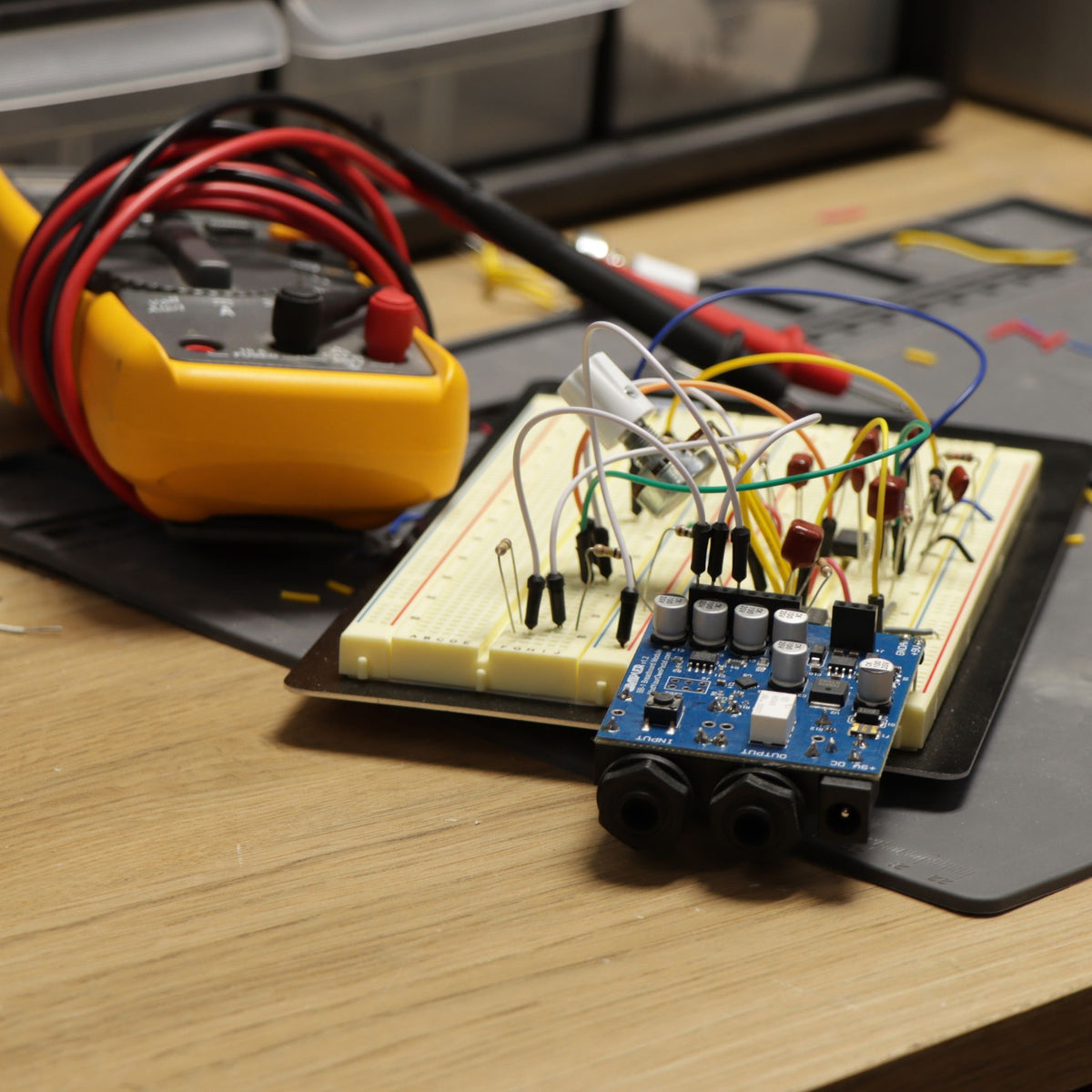 BB-1 guitar pedal breadboard module on a workbench, connected to a breadboard circuit next to a multimeter